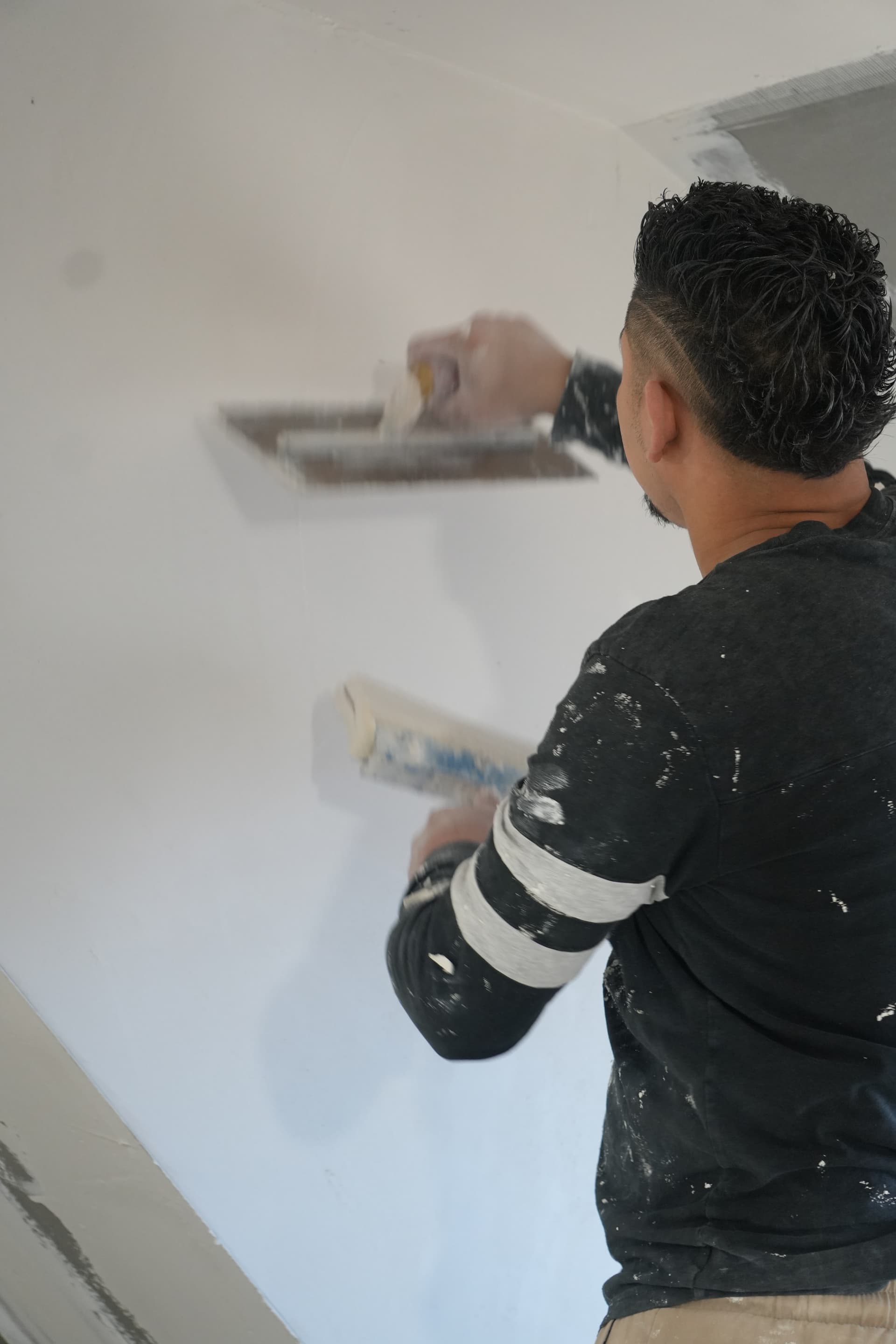 Crew member applying skim coat plaster to ceiling