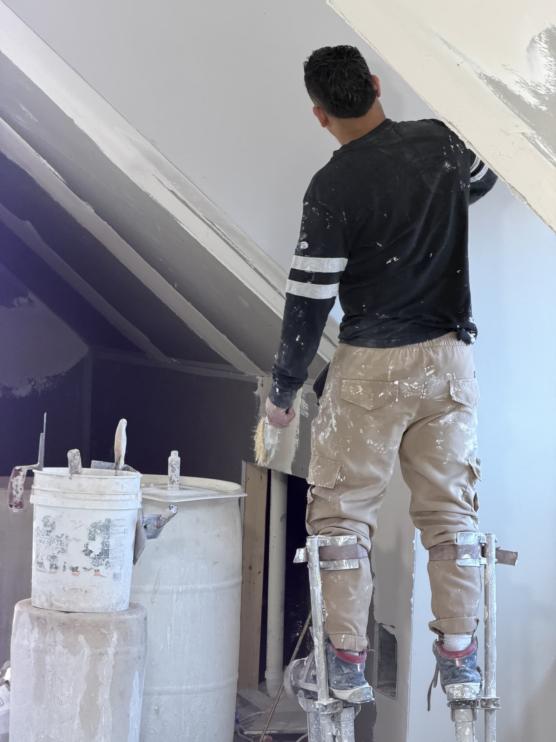 Worker on stilts plastering angled ceiling with bucket and tools