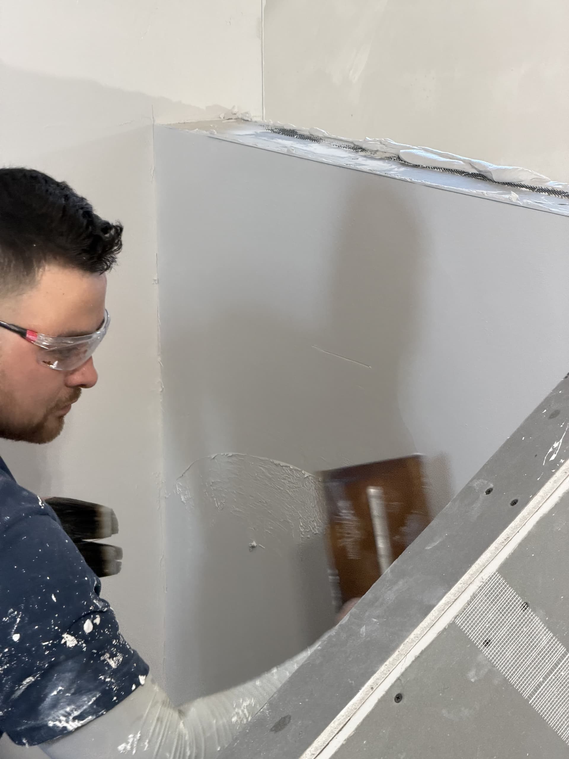 Plasterer applying finish coat — close-up detail with safety goggles