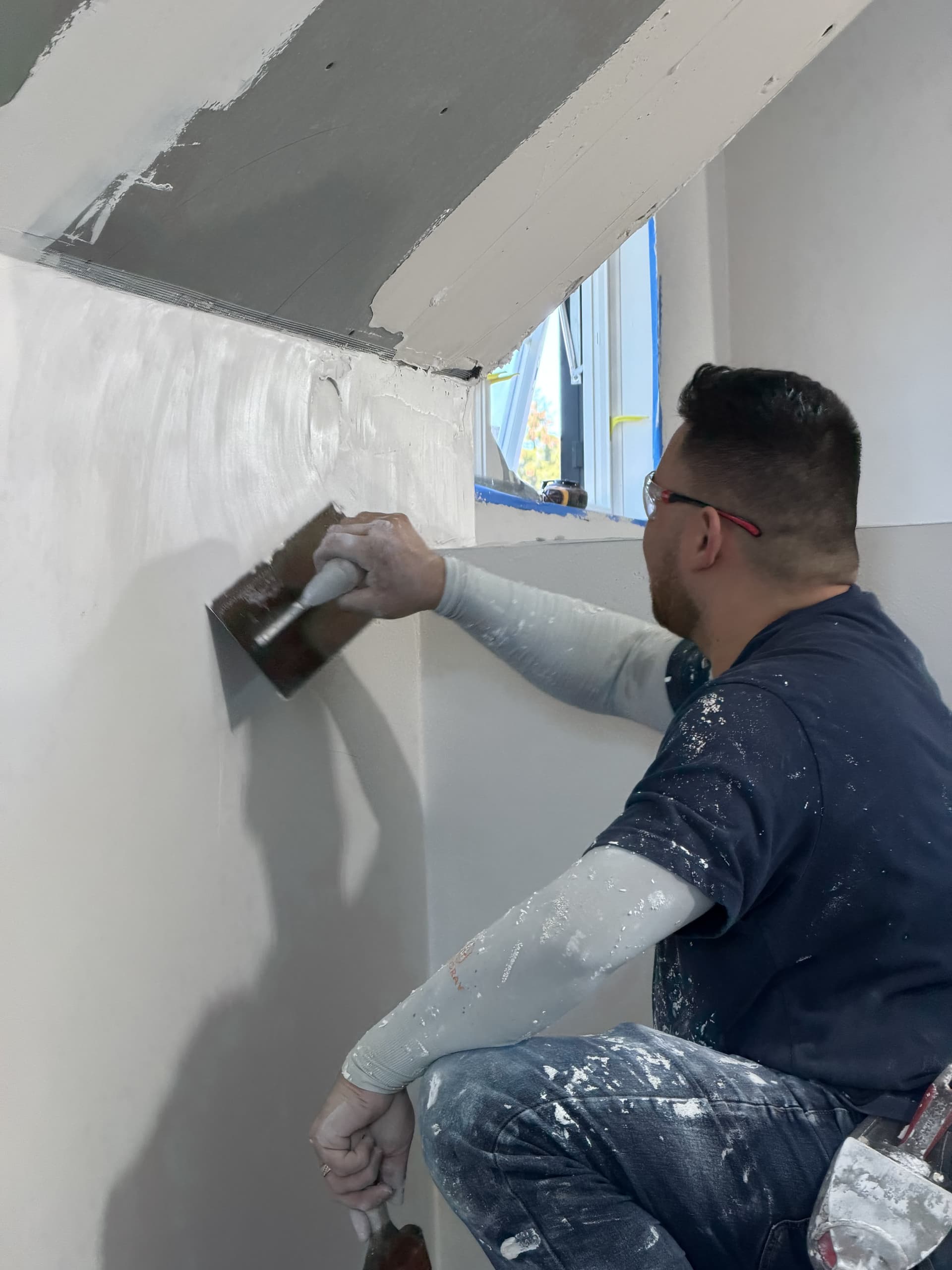 Worker applying smooth skim coat plaster to wall corner